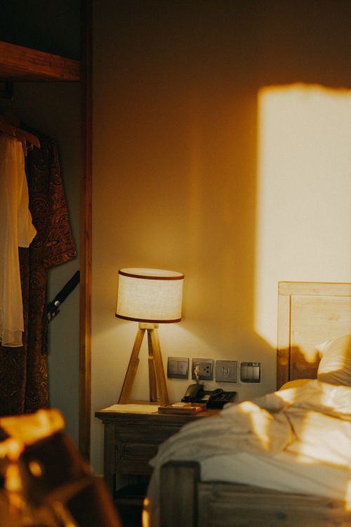 Free Sunlit bedroom with warm tones, featuring a neatly made bed and a stylish bedside lamp. Stock Photo