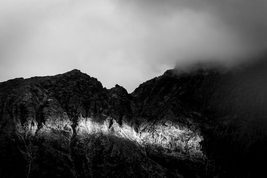 Breathtaking black and white photo of a rugged mountain range shrouded in clouds.