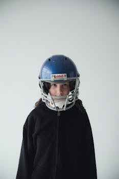 Portrait of a young girl wearing a blue football helmet with a white background.