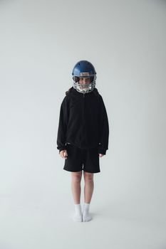 Child in sports gear with a blue helmet standing against a neutral background.