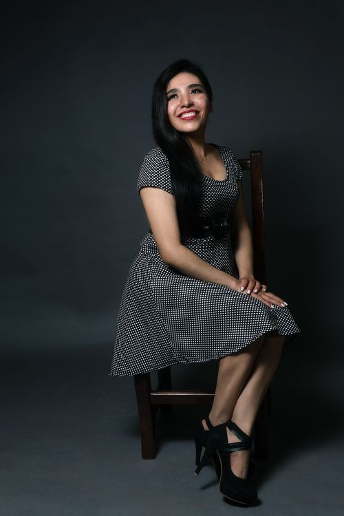 Free Smiling woman in a checkered dress posing elegantly on a chair in a studio setting. Stock Photo