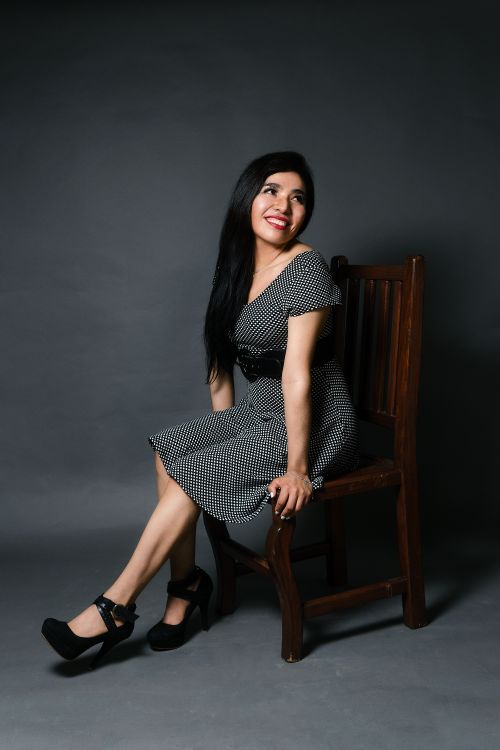 Free Charming woman with long black hair posing on a chair in a stylish black and white dress against a dark background. Stock Photo