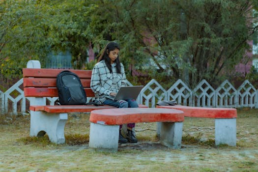 Young woman seated in a park working on her laptop, surrounded by greenery, Greater Noida, India.