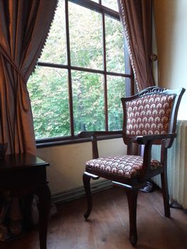 Elegant vintage armchair beside a window with draped curtains, offering a cozy room ambiance.
