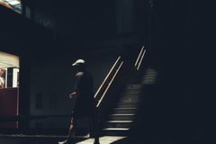 A man in casual wear walks through a dark, sunlit interior space, casting shadows.