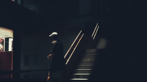 A man in casual wear walks through a dark, sunlit interior space, casting shadows.