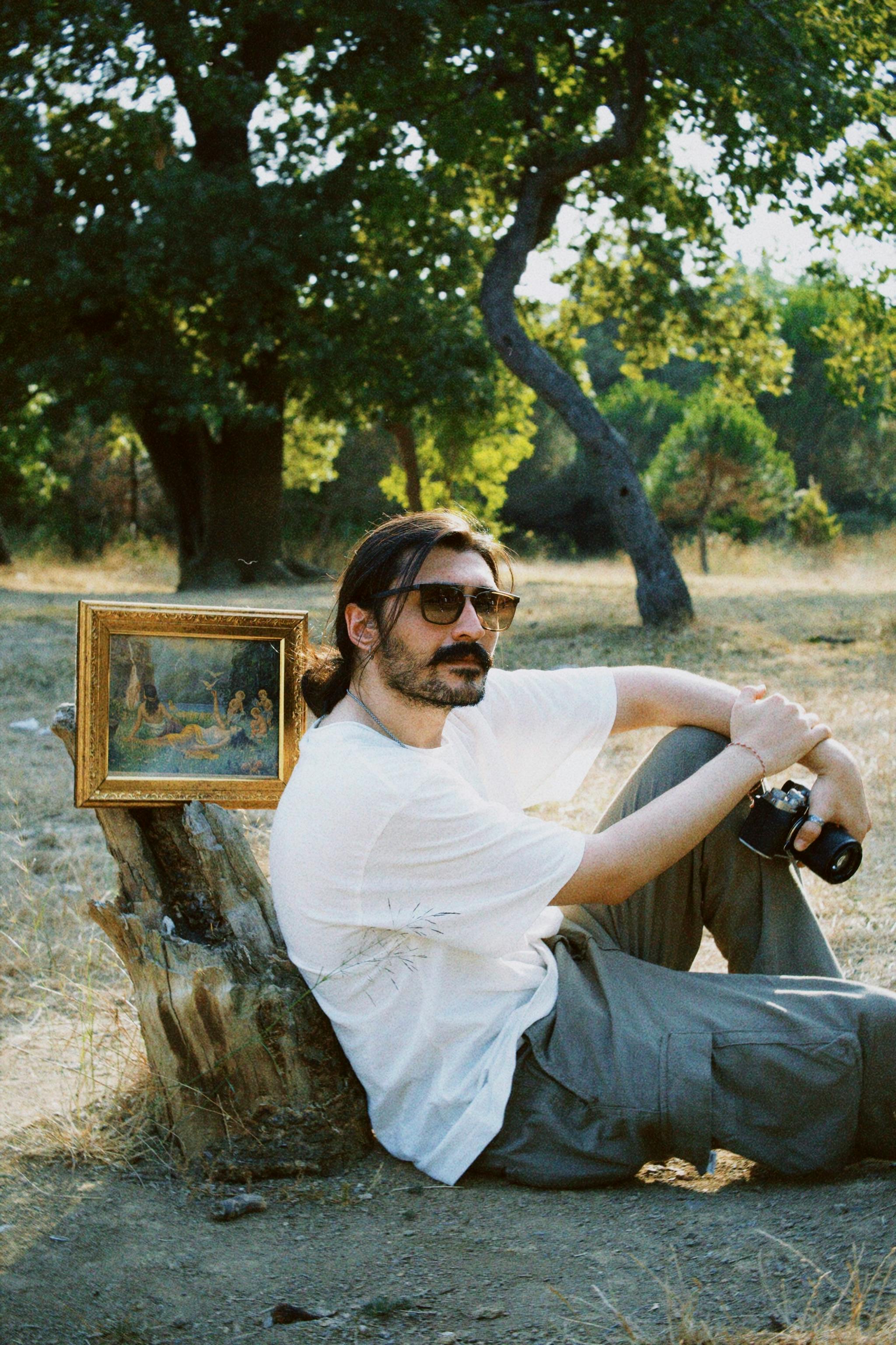 Man sitting outdoors by a framed painting, embracing nature and art.