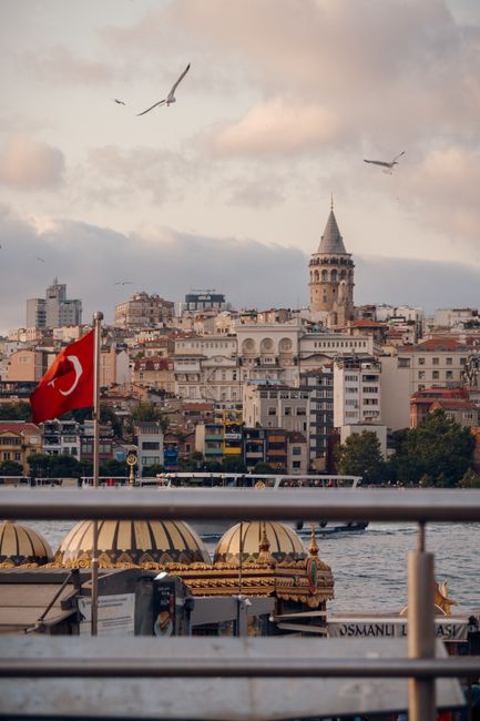 Scenic view of Galata Tower and vibrant Istanbul cityscape with Turkish flag and Bosphorus.