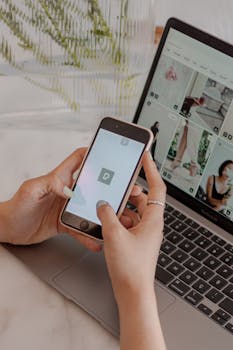 Close-up of hands using a smartphone and laptop for multitasking and digital browsing.