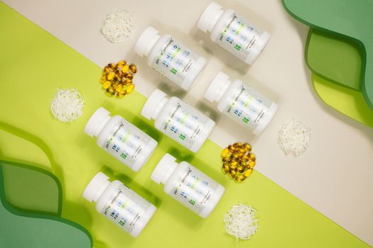 Flat lay of vitamin bottles with capsules and decorative elements against a green and white backdrop.