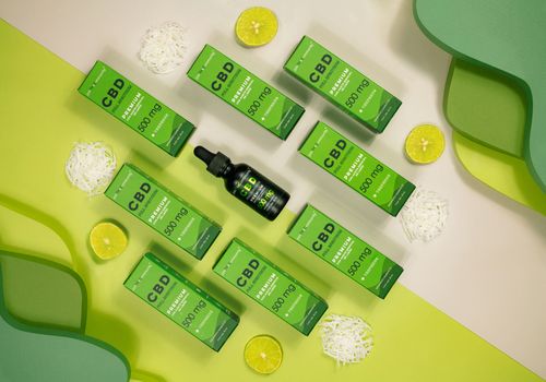 Free Top view of CBD product packaging with lime slices on a vibrant green background. Stock Photo