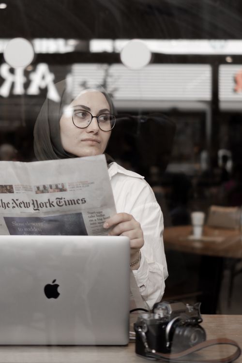 Free Woman in hijab reads a newspaper in a cafe, with a laptop and camera on the table. Stock Photo