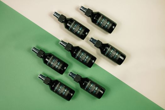 Stylish arrangement of cosmetic spray bottles on green and beige backdrop, perfect for product promotions.