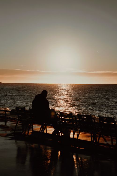 Free A person sitting on a bench watching a beautiful ocean sunset. Stock Photo