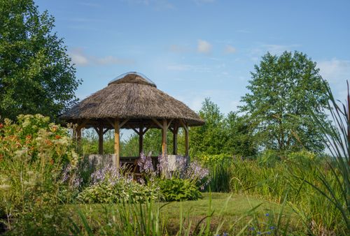 Free Idyllic summer scene with a thatched gazebo surrounded by lush greenery in rural Poland. Stock Photo