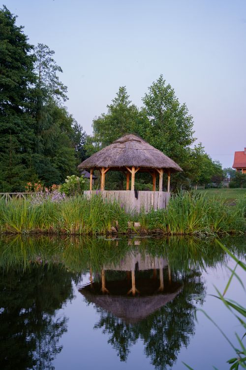 Free Serene lakeside view featuring a thatched gazebo and lush greenery in Dolistowo Nowe, Poland. Stock Photo