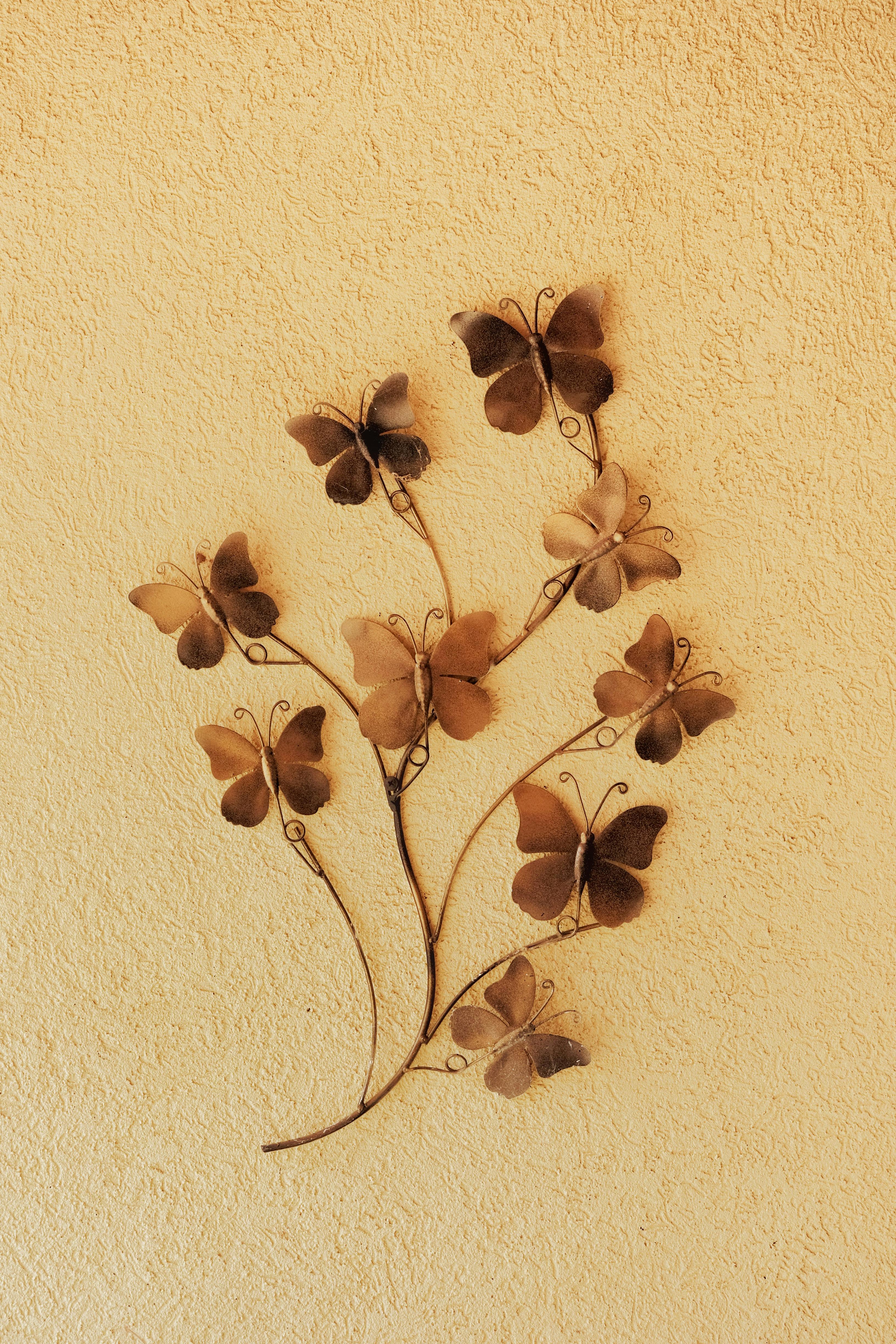 Artistic butterfly metal wall sculpture with detailed textures on a warm yellow background.