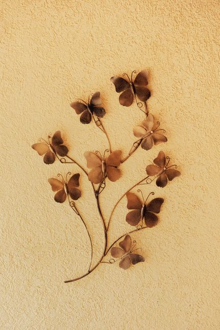 Artistic butterfly metal wall sculpture with detailed textures on a warm yellow background.