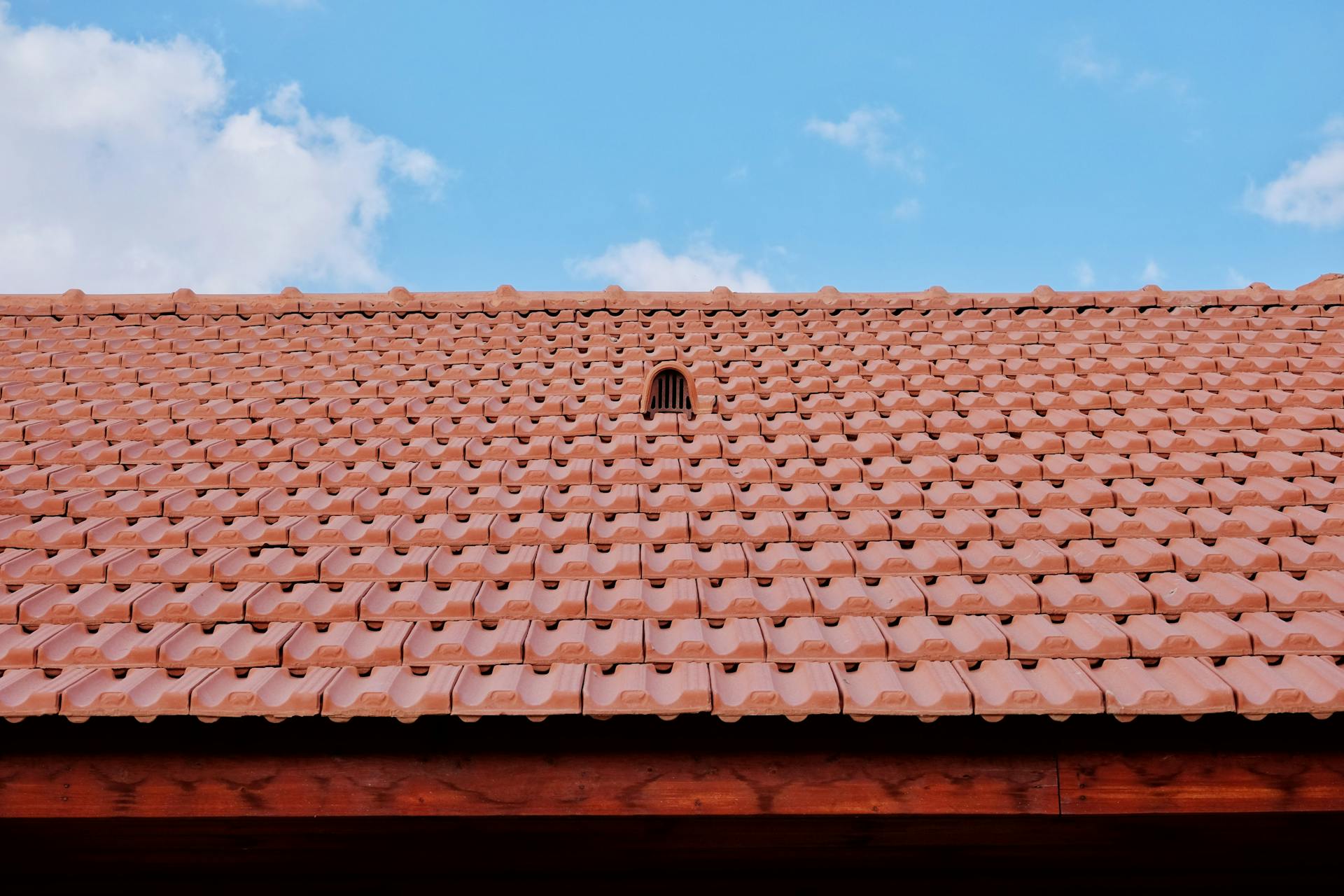 A detailed view of a red tiled roof with vent against a clear blue sky, showcasing architectural design.