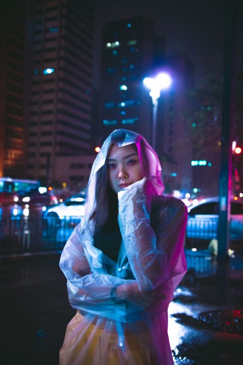 Free Woman in raincoat poses on city street at night with colorful lights and reflections. Stock Photo