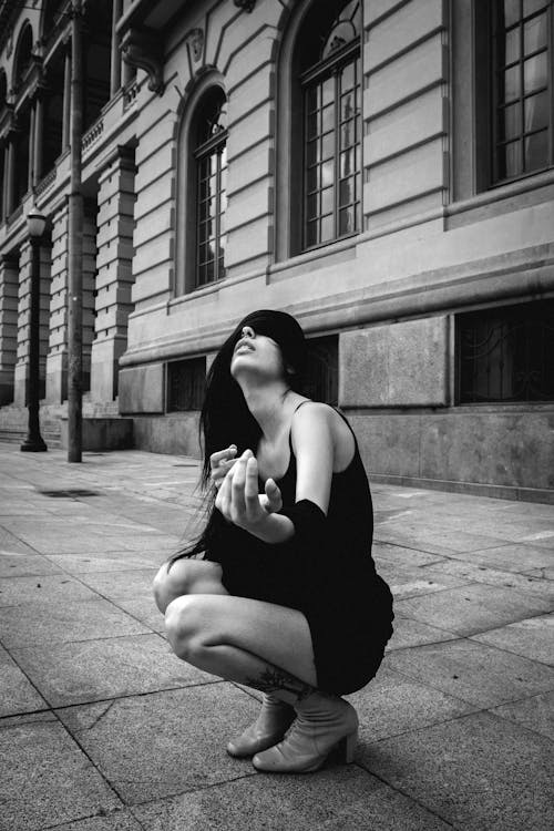 Free Woman Crouching on Pavement Near Building Stock Photo