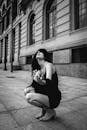Woman Crouching on Pavement Near Building