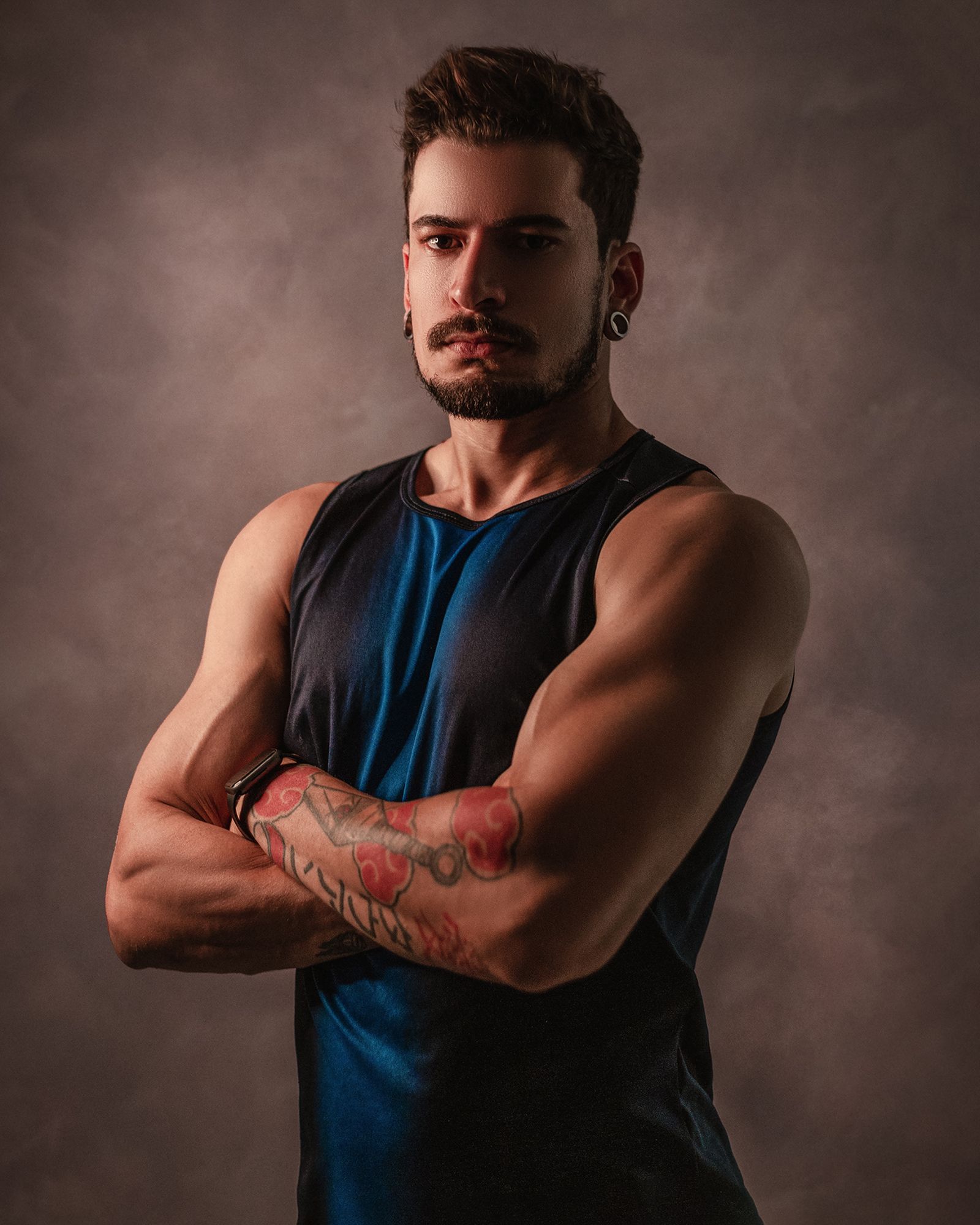 Portrait of a tattooed coach with his arms folded against a brown backdrop
