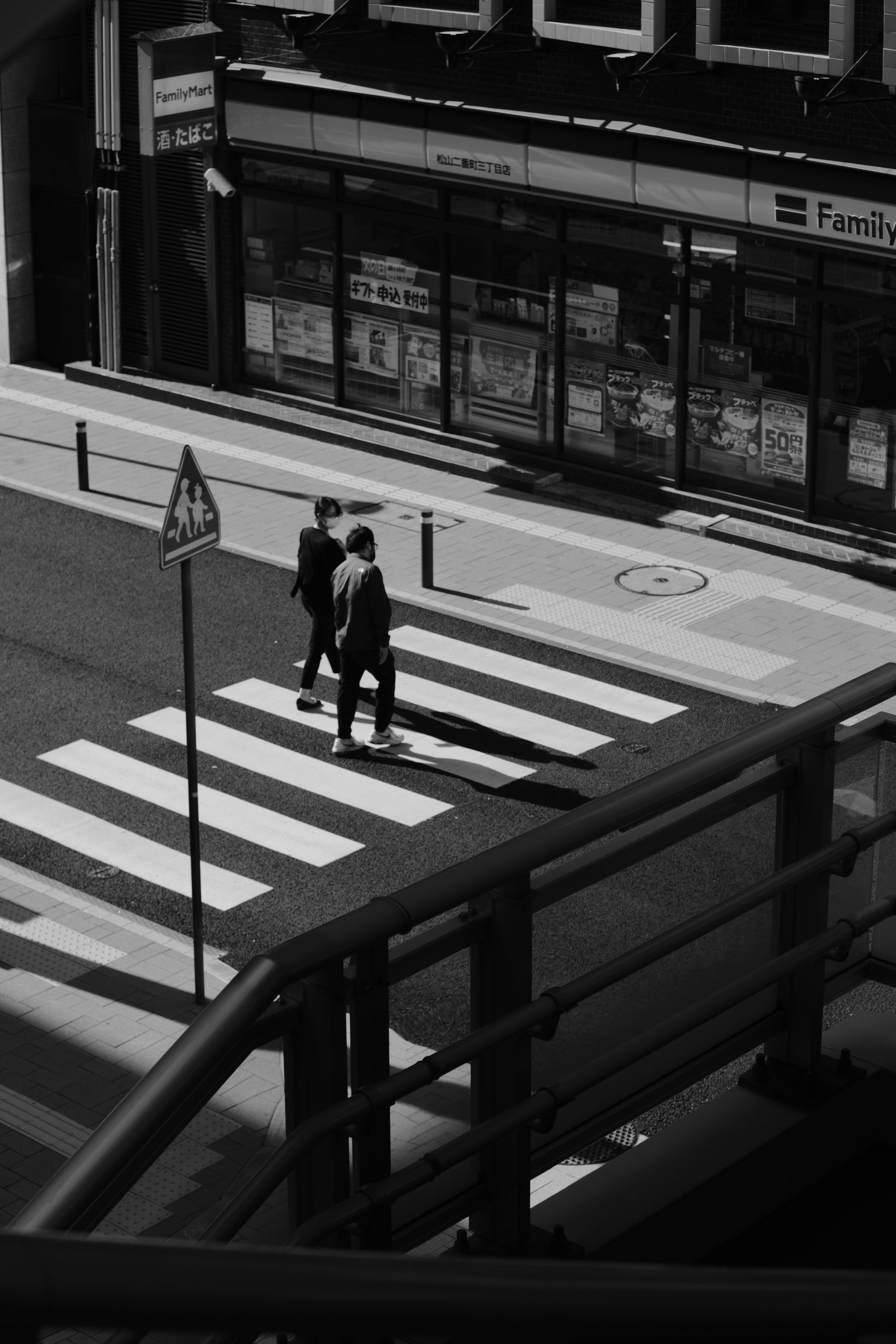 A high-angle view of two people walking on a city crosswalk in monochrome.