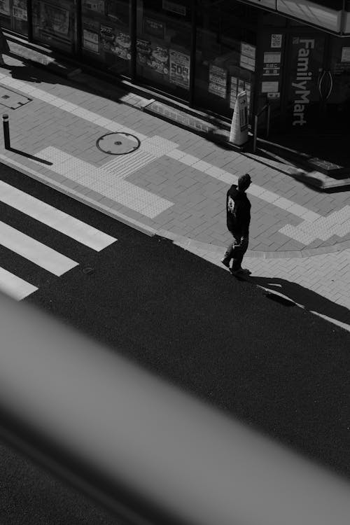 Black and White Photo of a Man Crossing the Street