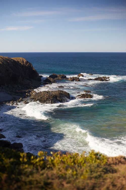 Free A breathtaking view of a rocky coastline with waves crashing against the shore under a clear blue sky. Stock Photo