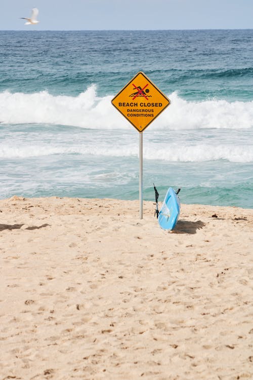A surfboard on the beach with a sign warning people to stay out of the water
