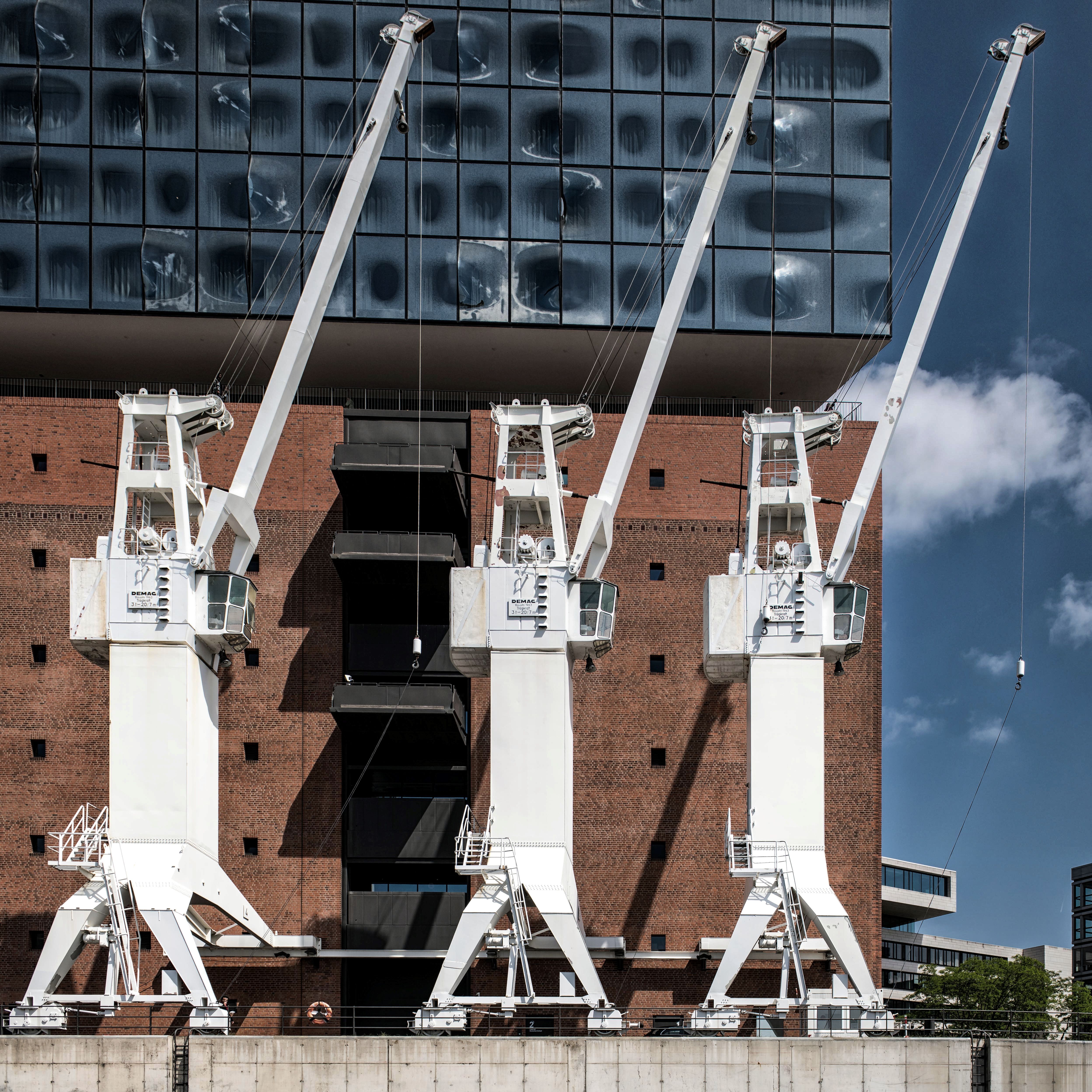 Three cranes against the Elbphilharmonie's glass facade in Hamburg's urban waterfront.