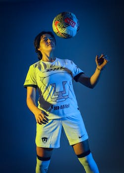 Athletic woman in sportswear juggling a soccer ball against a blue background.