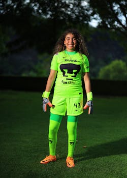 A woman wearing bright green sports gear stands on a grassy field with trees in the background.