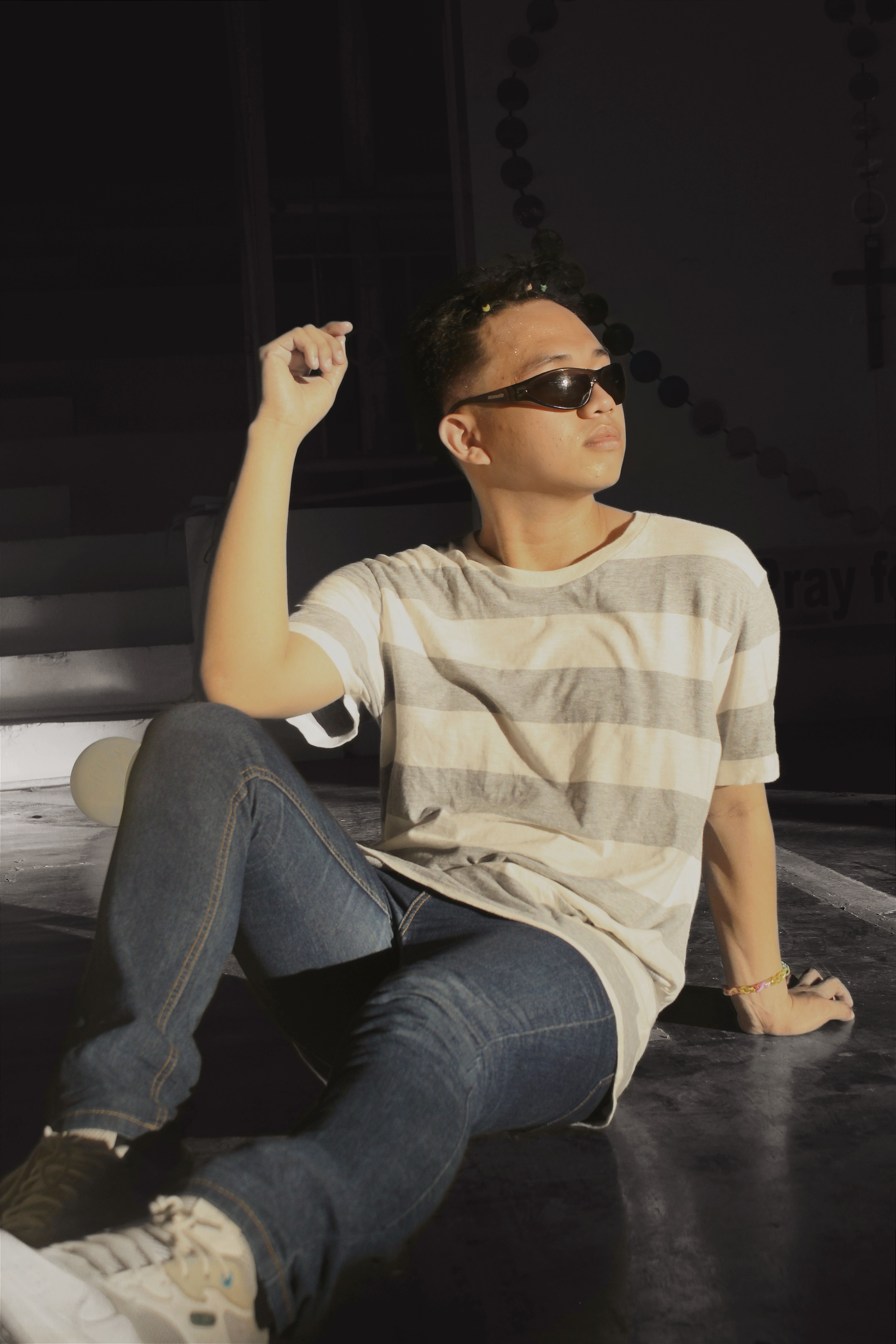Casual young adult sitting indoors with sunglasses, capturing modern style in sunlight.