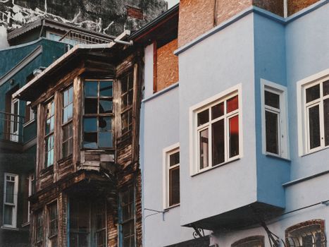 Juxtaposition of a decaying wooden house with a newly painted modern building in an urban setting.