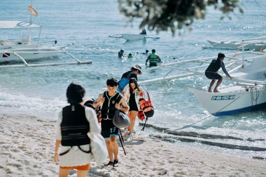 Group of tourists preparing for a boat ride on a sandy beach with clear blue waters.