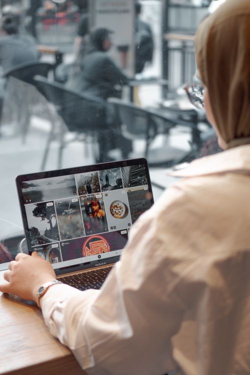 Free A young woman uses a laptop to browse social media in a cozy café setting. Stock Photo