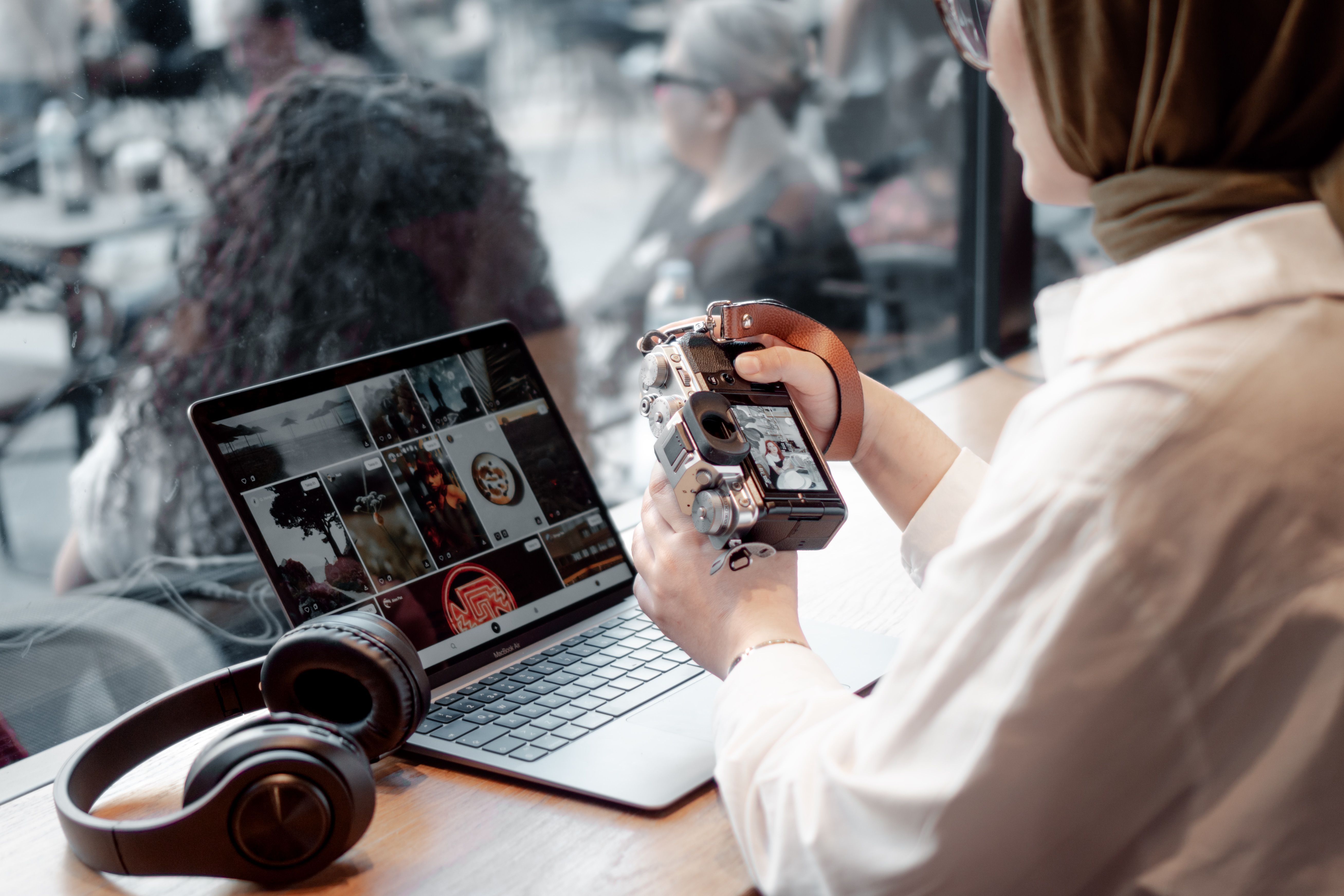 A photographer edits photos on a laptop in a café, with a smartphone nearby.