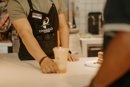 A barista wearing an apron serves an iced coffee to a customer inside a coffee shop.