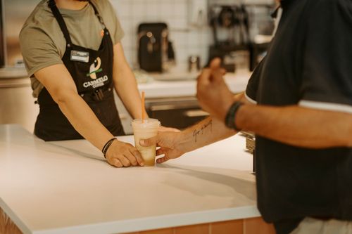 Free Barista hands cold drink to customer in cozy café setting, showcasing hospitality. Stock Photo