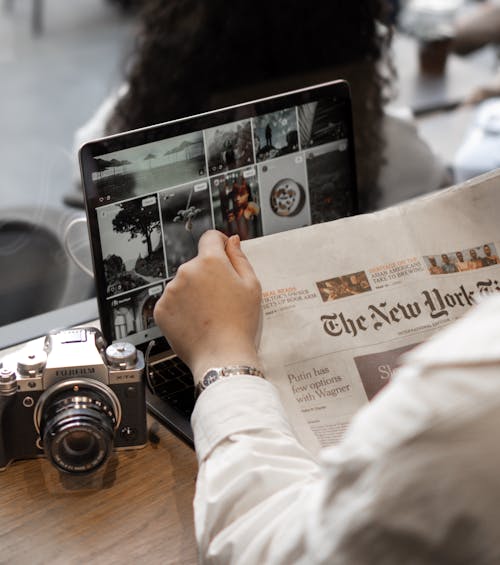 Person reading a Newspaper and Using a Laptop and a Camera 