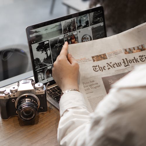 Free Hand Holding New York Times near Camera and Laptop Stock Photo