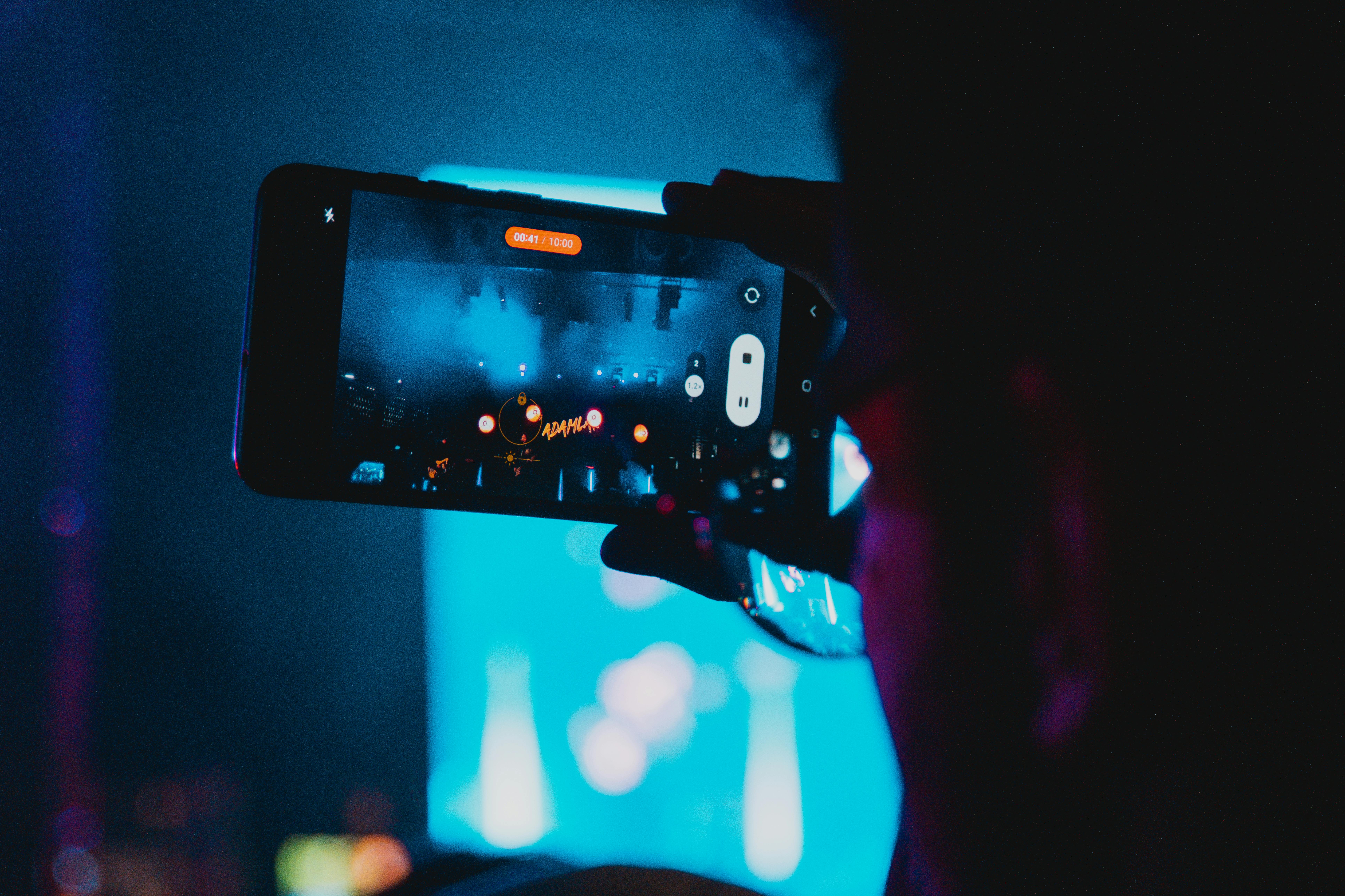 Close-up of a person filming a concert with a smartphone, capturing vibrant stage lights and atmosphere.