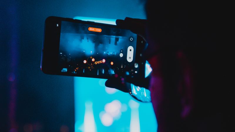 Close-up of a person filming a concert with a smartphone, capturing vibrant stage lights and atmosphere.