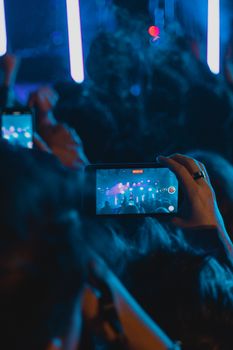 Concert crowd capturing live performance on smartphones with vibrant lights.