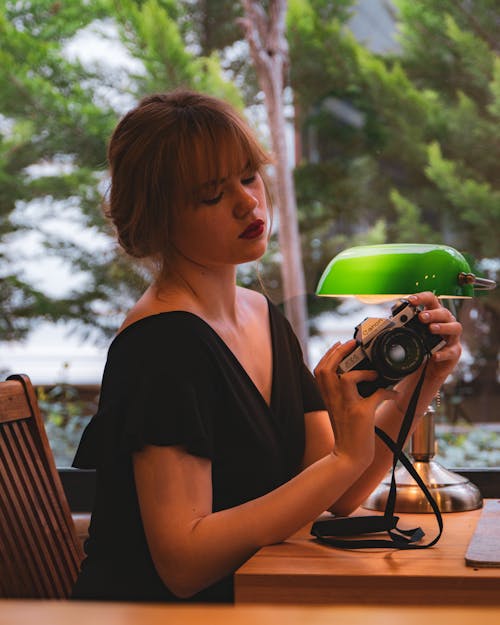 Young Woman Sitting at a Desk and Holding a Camera 