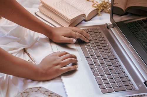 Free Close-up of a woman typing on a laptop surrounded by open books and a notebook. Stock Photo