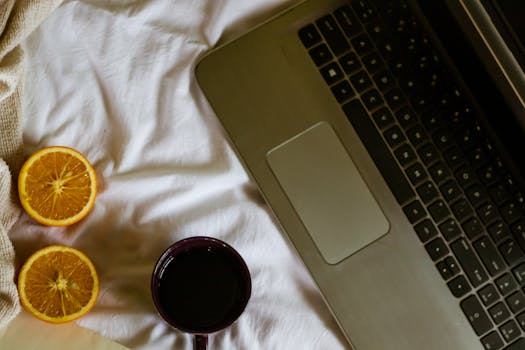 A cozy setup featuring a laptop, coffee mug, and sliced oranges on a bed, ideal for relaxed work from home.