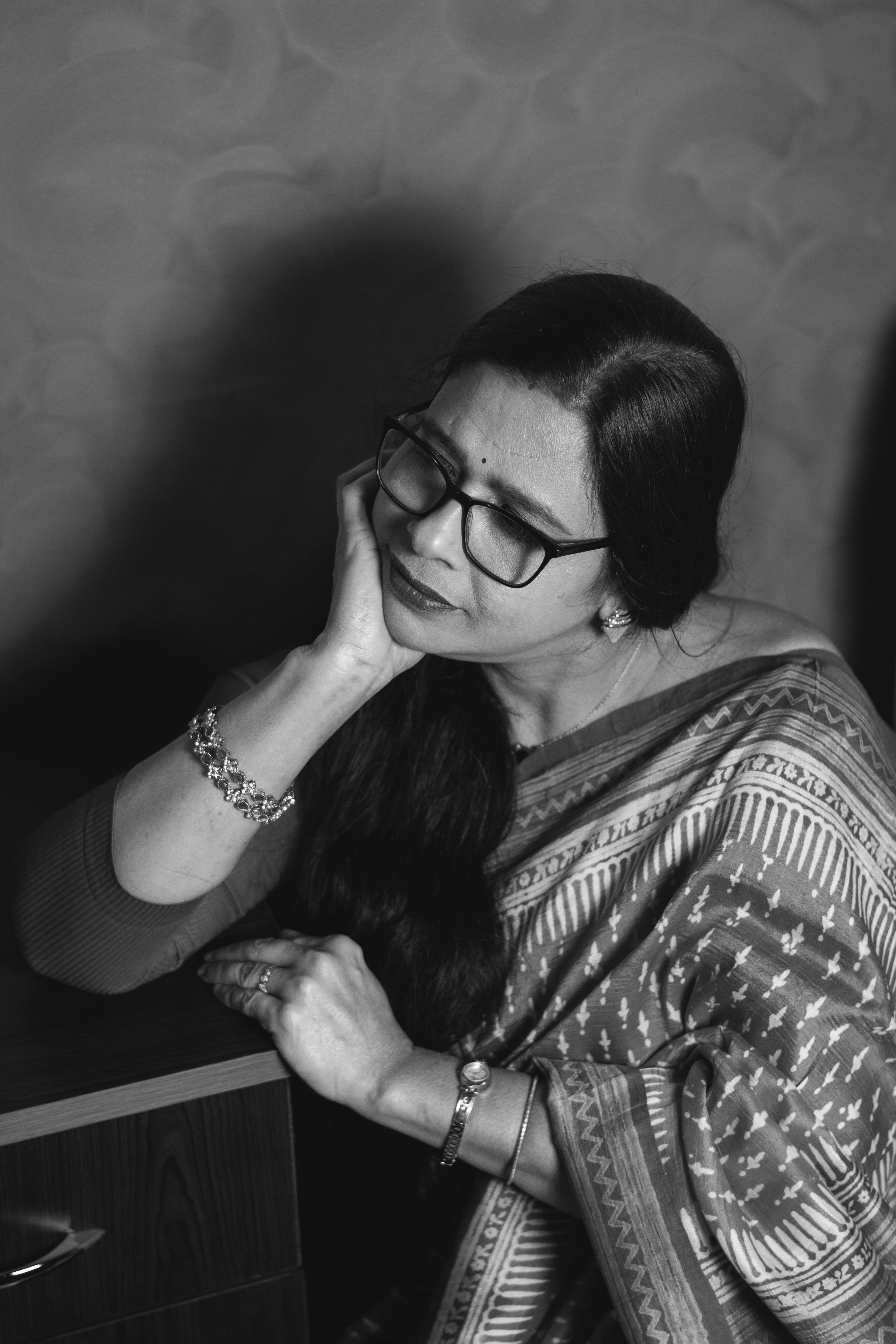 Black and white portrait of an adult woman wearing a sari and eyeglasses, sitting indoors.